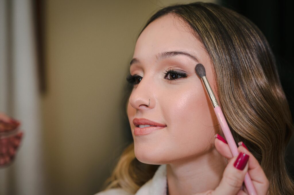 Close-up of a young woman applying makeup with a brush, showcasing beauty and elegance.